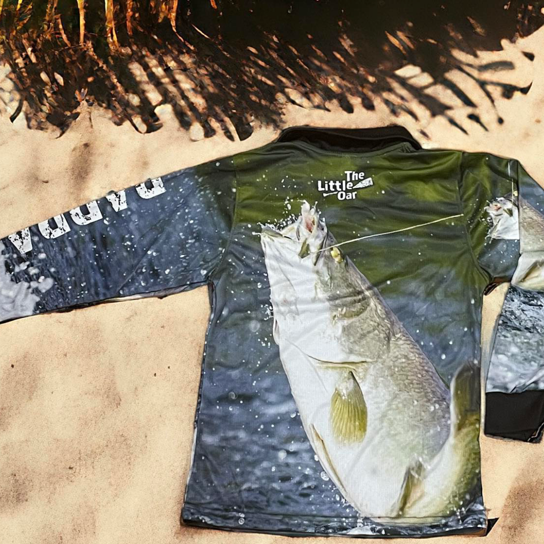 The Dirty Oar Barra Kids Fishing Shirt on sand background.