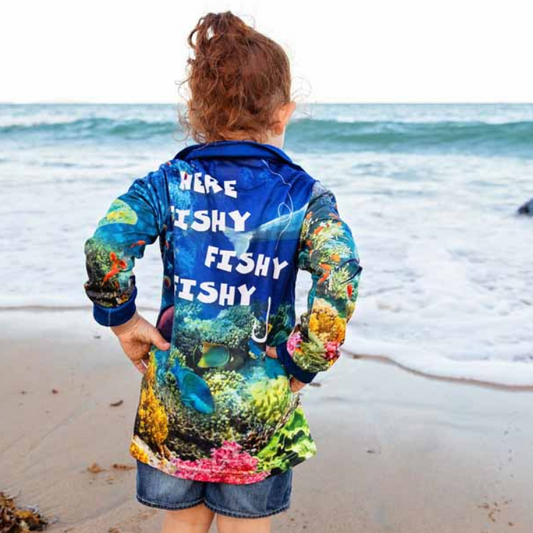 A child standing on a beach wearing The Dirty Oars The Reef Kids Fishing Shirt. Shirt Back