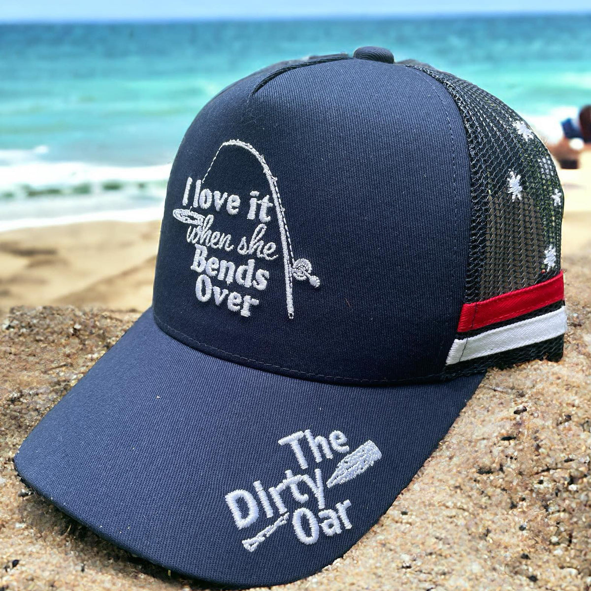 This image features a navy blue trucker hat with a playful and cheeky embroidery that reads, "I like it when she bends over" in white letters, positioned prominently on the front panel. The hat also displays a small, distinctive logo that reads "The Dirty Oar" on the brim, adding a unique touch. Bend Over Aussie Trucker Cap