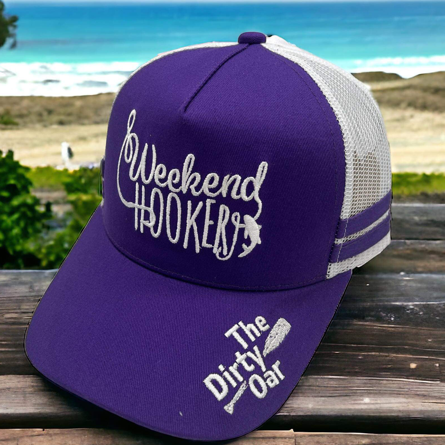 A purple trucker hat with a mesh back, featuring white text 'Weekend HOOKER' on the front and 'The Dirty Oar' on the side. The hat has a ponytail hole at the top.