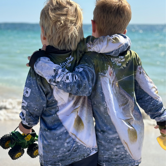 Two children wearing The Dirty Oar Barra Kids Fishing Shirt, standing by the sea.