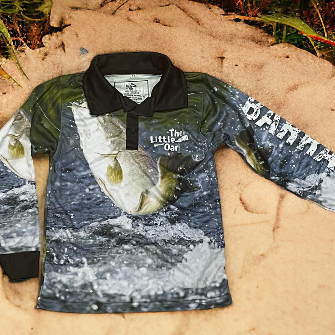 The Dirty Oar Barra Kids Fishing Shirt on sand background.