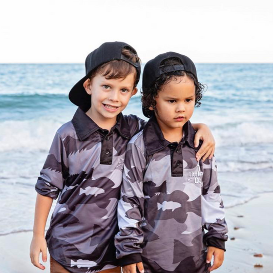 Two children wearing The Dirty Oar Coral Trout Kids Fishing Shirts, standing on a beach.