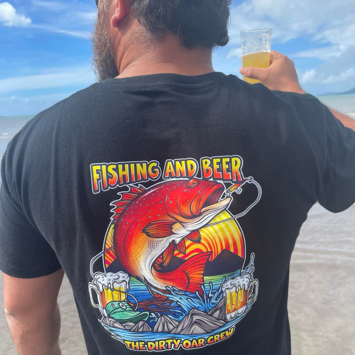 A person standing on a beach, having a beer, wearing a Fishing & Beer T-Shirt.