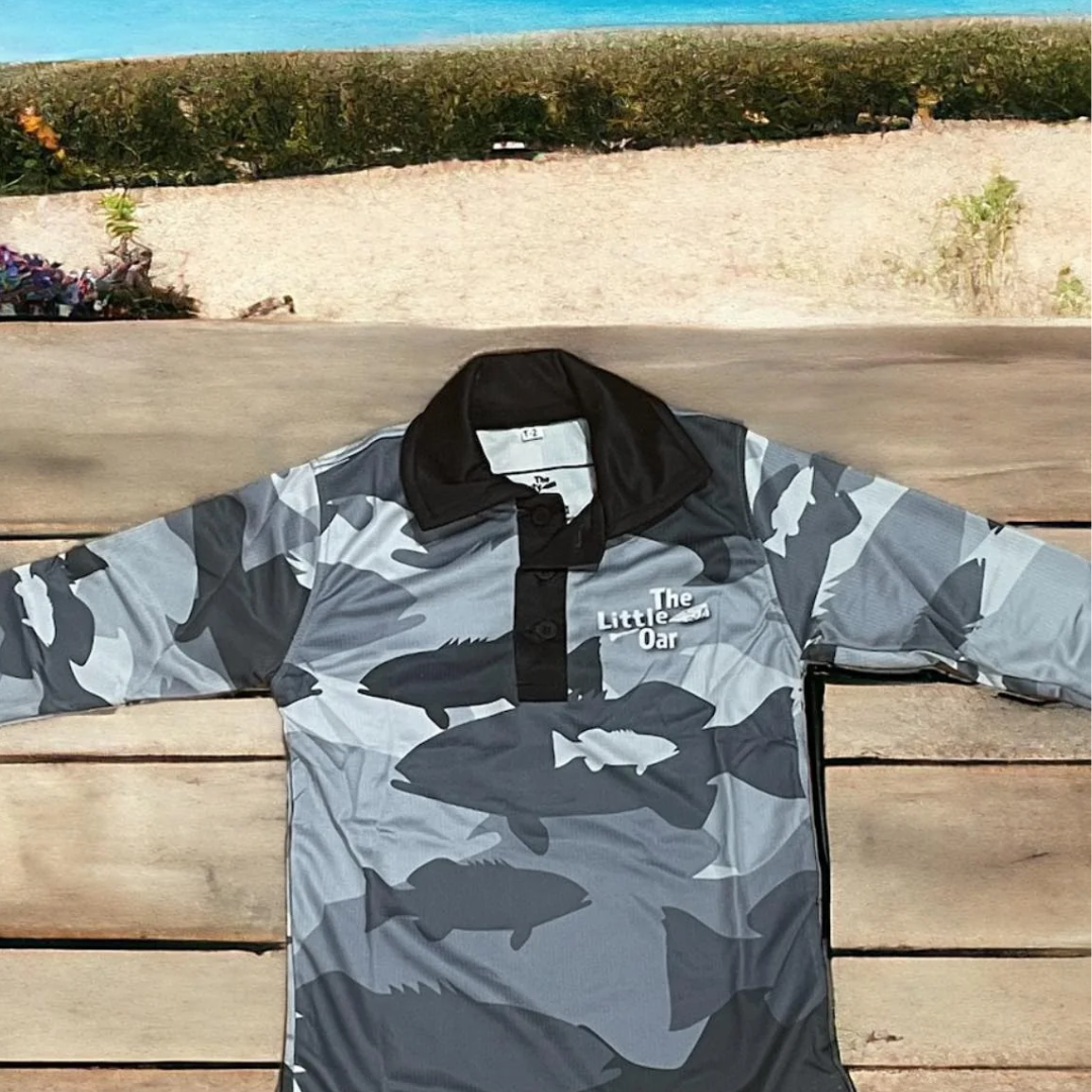 The Dirty Oar Coral Trout Kids Fishing Shirt, on wooden background.