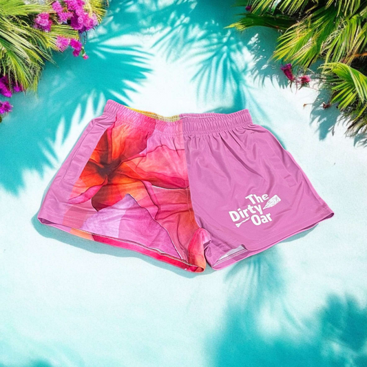 The Dirty Oars Frangipani Womens Shorts on sandy background with pink flowers and green leaves.