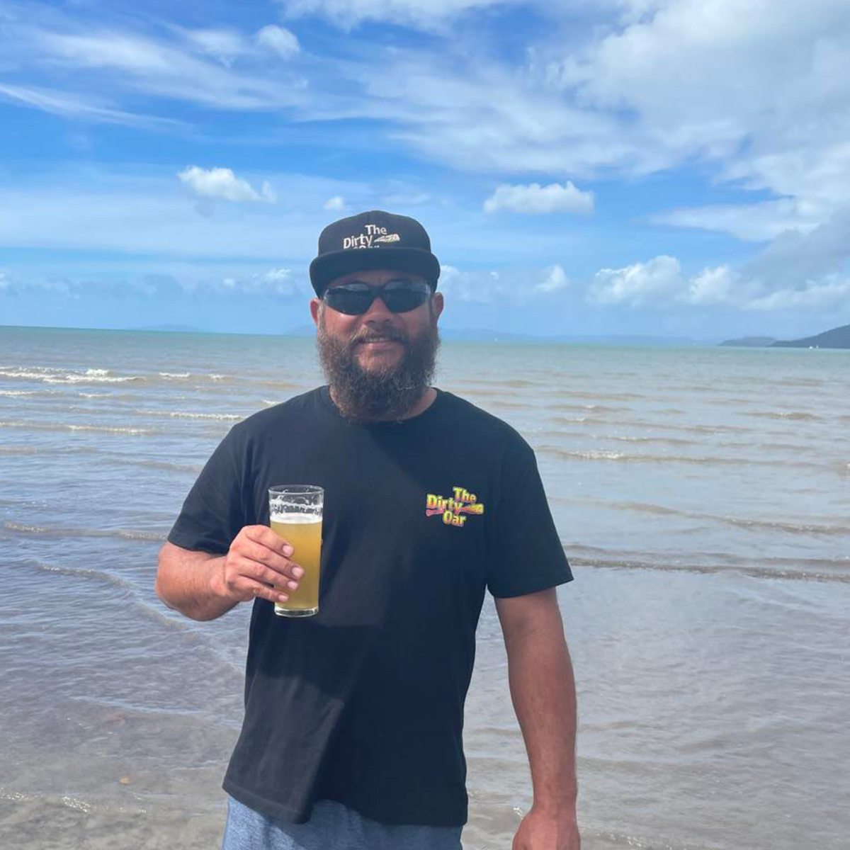 A person standing on a beach, having a beer, wearing a Fishing & Beer T-Shirt.