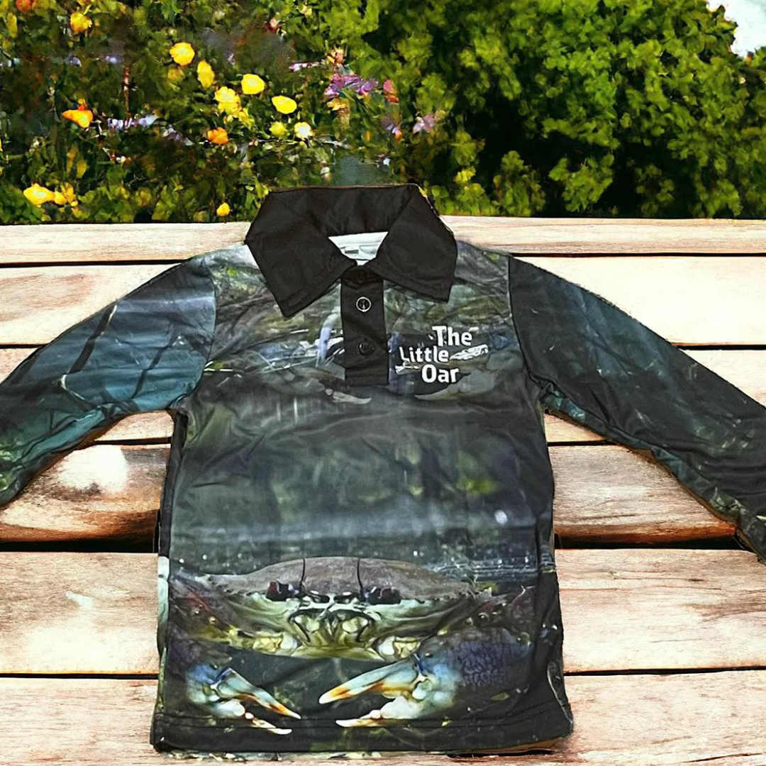 The Dirty Oars Mud Crab Kids Fishing Shirt on a wooden background with some flowers.