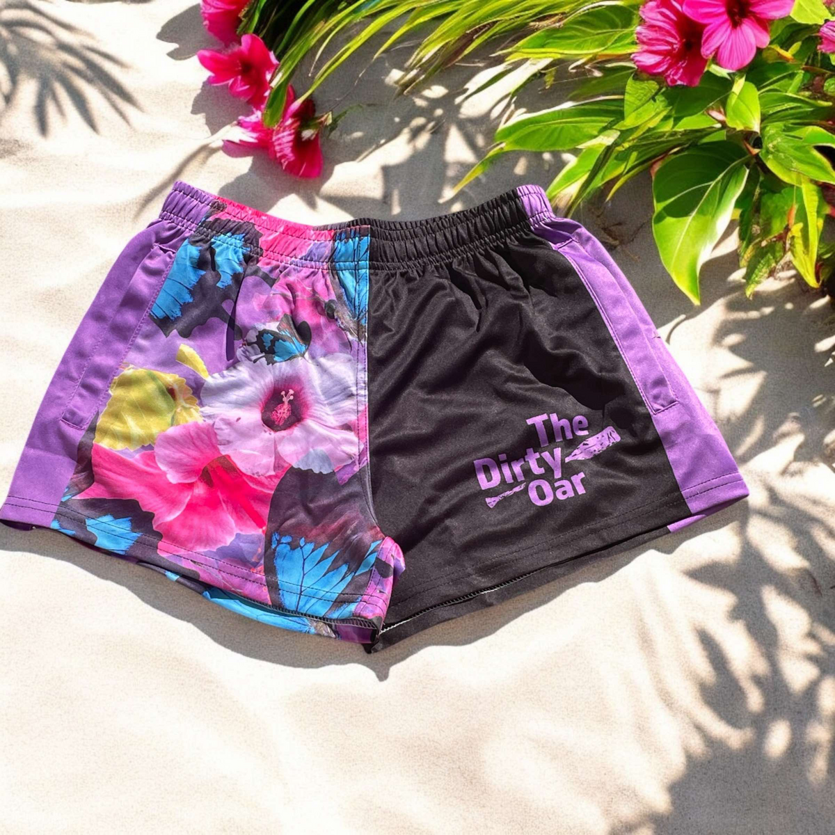 The Dirty Oar Princess womens shorts , on a sandy background with hibiscus and green leaves.