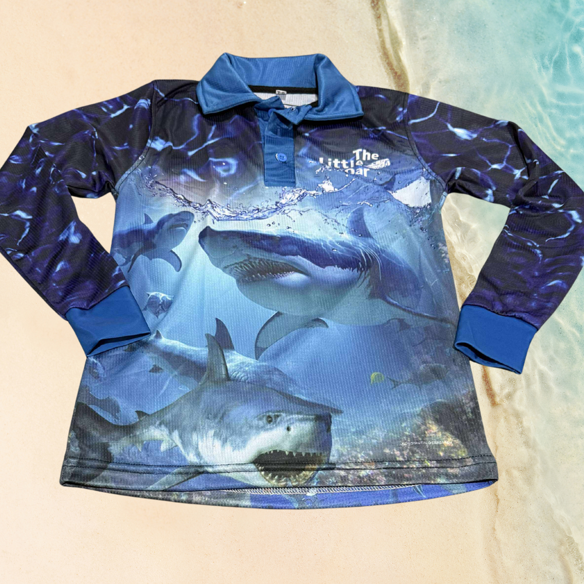 The Dirty Oar Taxman Kids Fishing Shirt has a shark design with a sandy background.