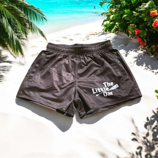 The Dirty Oar Kids Shorts on a sandy bak ground with green leaves orange flowers and crystal blue water.