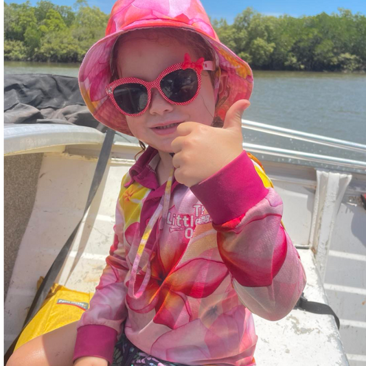 Litthe girl on boat wear The Dirty Oars Frangipani Kids Fishing Shirt and frangpani bucket hat with sun glasses.