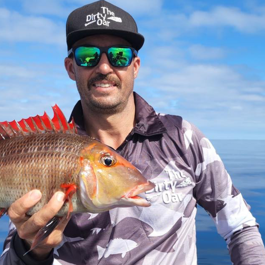Man Holding a red throat emperor wearing The Dirty Oars Coral Trout Mens Fishing Shirt and The Dirty Oar Flat Bream Cap.