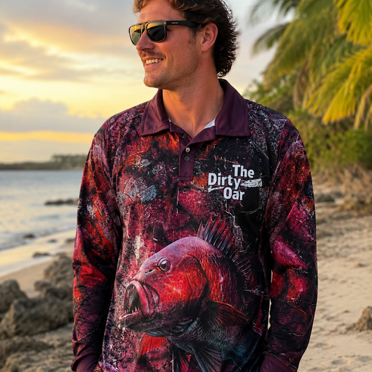 A man wearing The Dirty Oar Mangrove Jack Mens Fishing Shirt stands on a sandy beach at sunset. 
