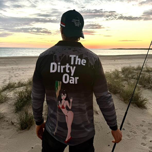 Man standing on beach wearing The Dirty Oars Men’s fishing shirt black and I love it when she bends over Trucker cap.