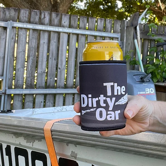 A can holder with 'The Dirty Oar' branding is attached to a surface, presumably a beverage inside. The holder is dark-colored and there's outdoor fencing in the background.